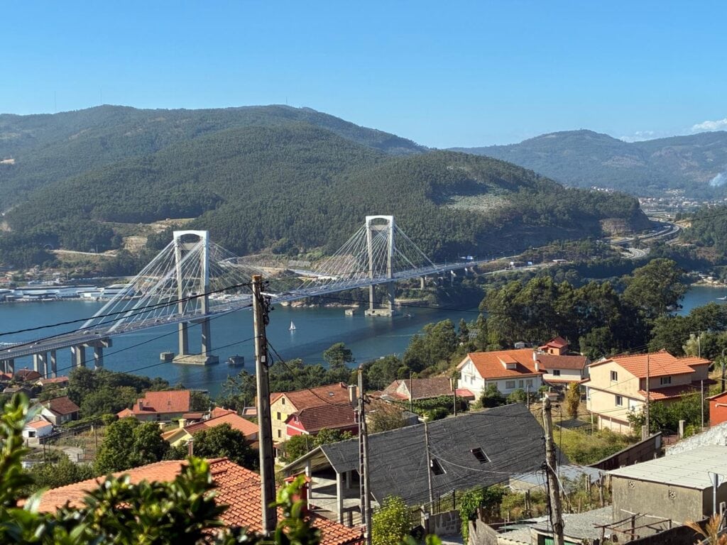 Scenic view of a bridge over a river with houses and mountains in Galicia, Spain.