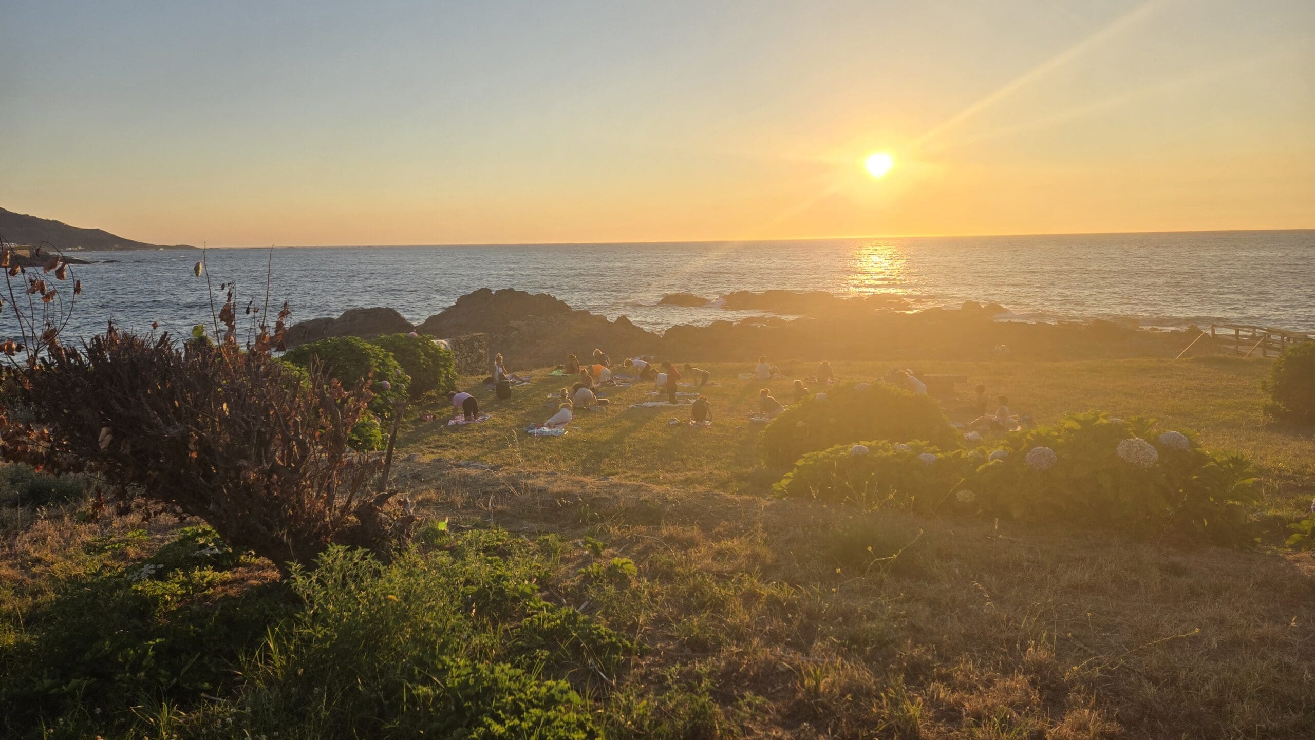 Sunset over the Galician coast with rocky shoreline and lush greenery.