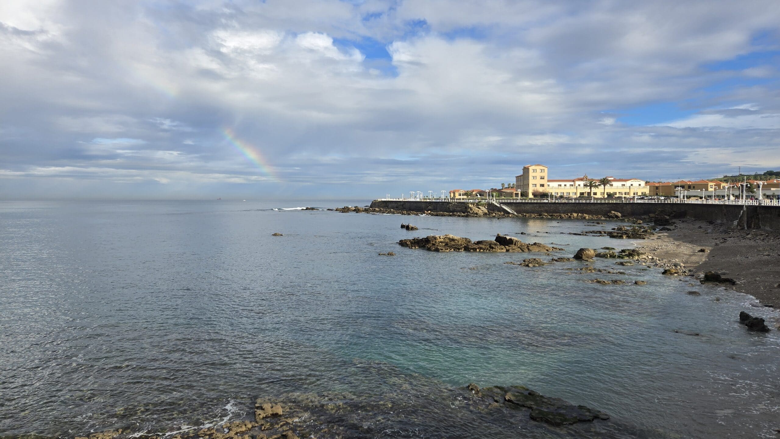 Scenic view of the Galician coast with rainbow and cloudy sky.