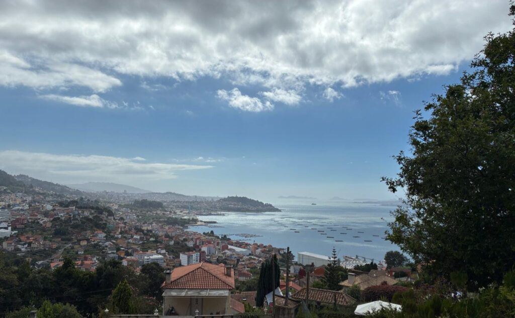 Scenic view of the Galician coastline with houses and the Atlantic Ocean under a partly cloudy sky.