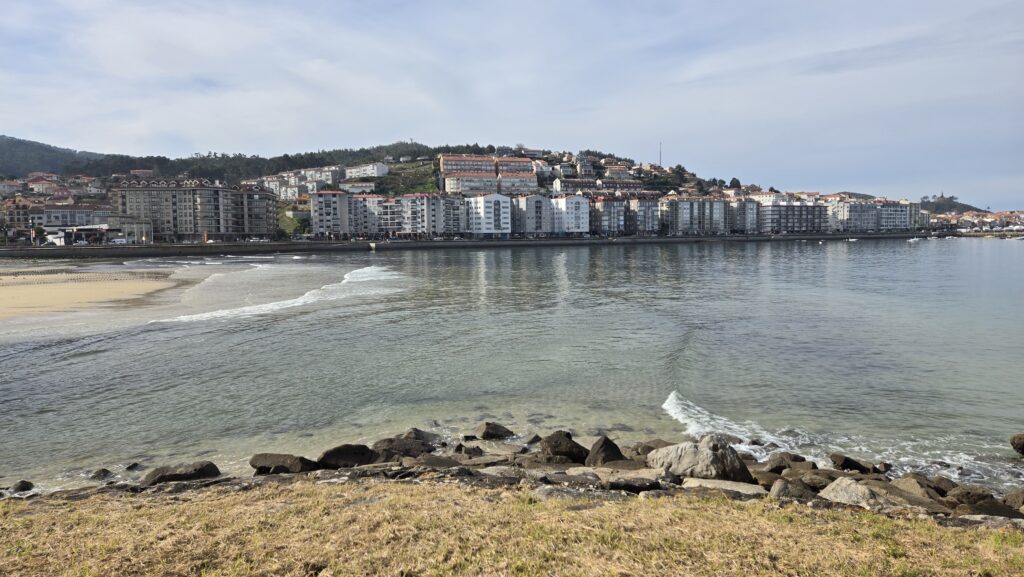Scenic view of a coastal city in Galicia with beach and hillside buildings.