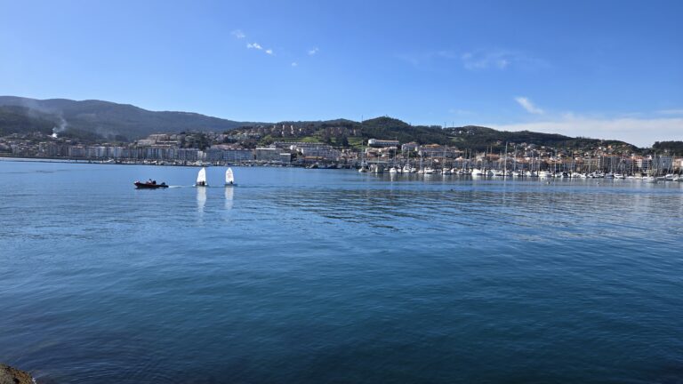Scenic view of a calm bay with sailboats and a cityscape in Galicia, Spain.