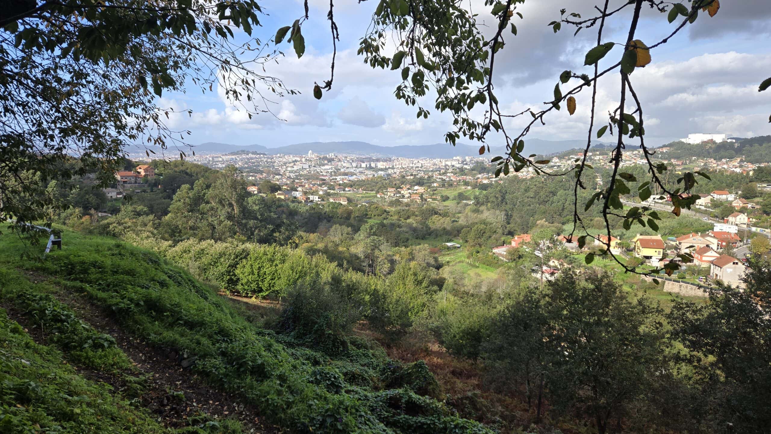 Scenic view of Galicia with lush greenery and distant townscape under a partly cloudy sky.