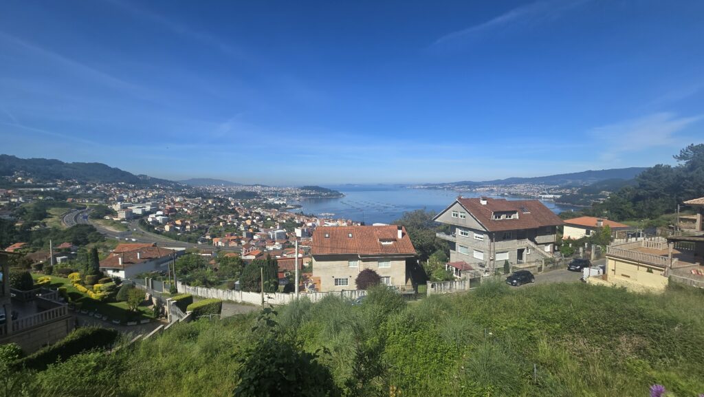 Scenic view of Galicia with houses, hills, and a bay under a blue sky.