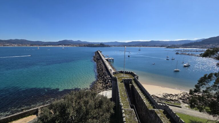 Scenic view of a harbor with boats and a stone pier in Galicia, Spain.