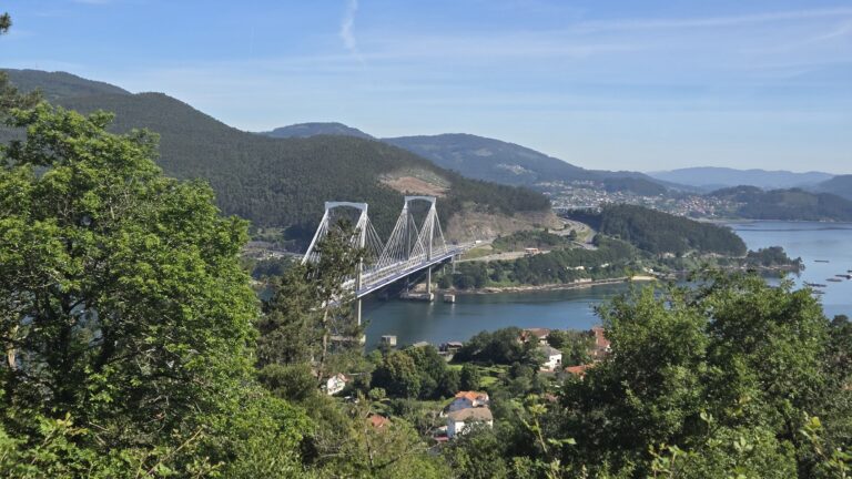 Scenic view of a bridge over a river surrounded by lush green hills in Galicia, Spain.