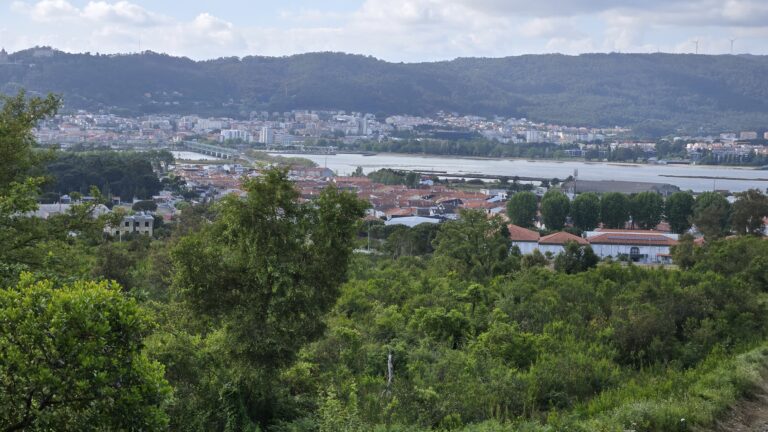 Scenic view of a city by a river with lush green hills in Galicia, Spain.